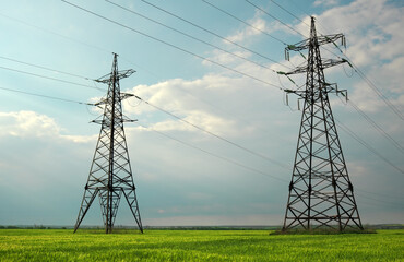 High voltage lines and power pylons in a flat and green agricultural landscape on a sunny day with clouds in the blue sky. Cloudy and rainy. Wheat is growing