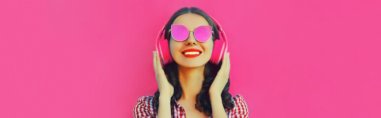 Portrait of happy smiling woman listening to music with headphones wearing pink sunglasses on background