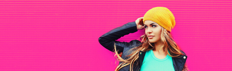Portrait of beautiful blonde young woman looking away wearing yellow hat, black rock jacket on pink background