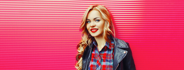Portrait of beautiful blonde young woman with red lipstick wearing black rock jacket on pink...