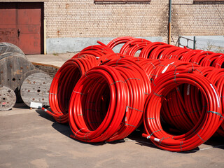 A large number of red pvc pipes lie twisted into huge rolls