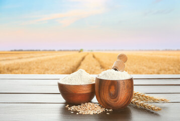 Bowls with fresh wheat flour on wooden table in field
