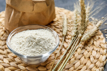 Bowl with flour and wheat ears on wicker mat, closeup