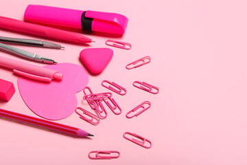 Pink paper clips with stationery supplies on color background