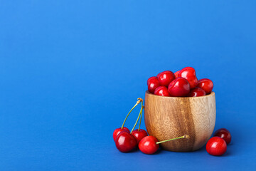 Wooden bowl with sweet cherries on blue background