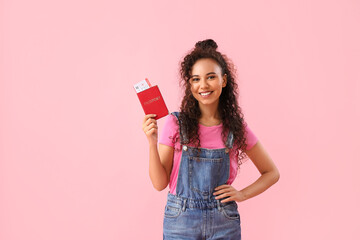 Young African-American woman with passport and ticket on pink background