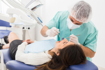Dentist man examining a latin female patient teeth with dental tools - mirror and probe