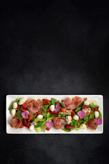 Salad with prosciutto, strawberries and mozzarella, on a dark. vertical