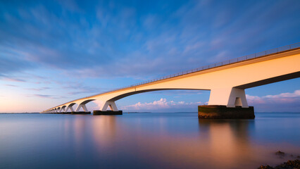 A long bridge over the sea during sunset. Long exposure photo. Landscape during a bright sundown. The sea and the bridge. Zeeland bridge, Netherlands.