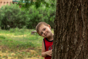 cute preschool boy peeking out from behind a tree in the park