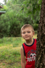 cute preschool boy peeking out from behind a tree in the park