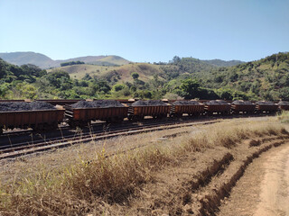 Landscape showing train loaded with ore in the foreground and hills and mountains under clear blue...