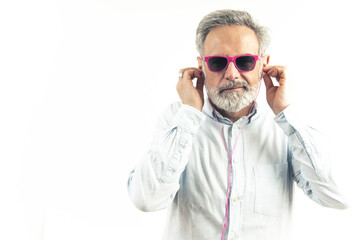 grey-haired Caucasian man in pink sunglasses listens to music in pink earphones white background studio shot copy space indoors . High quality photo