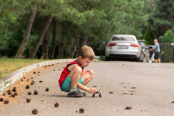 a boy plays toy car assembled from designer parts. He is  in a red T-shirt against the background of green bushes and trees