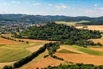 Fototapeta na wymiar Der Bergfried der Höhenburg Vetzberg auf einem Vulkanberg in Mittelhessen, eingebettet in eine landwirtschaftlich genutzte Landschaft mit leicht bewölktem Himmel am Horizont bei schönem Sommerwetter