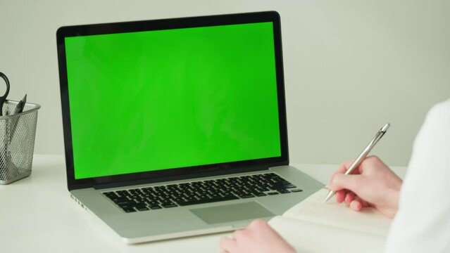 Computer laptop with chroma key close-up. Green screen on monitor. Doctor workplace, woman nurse working. Distance education, e-learning. 