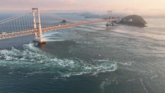 Aerial: Pullback on whirlpools under Naruto suspension bridge at sunset