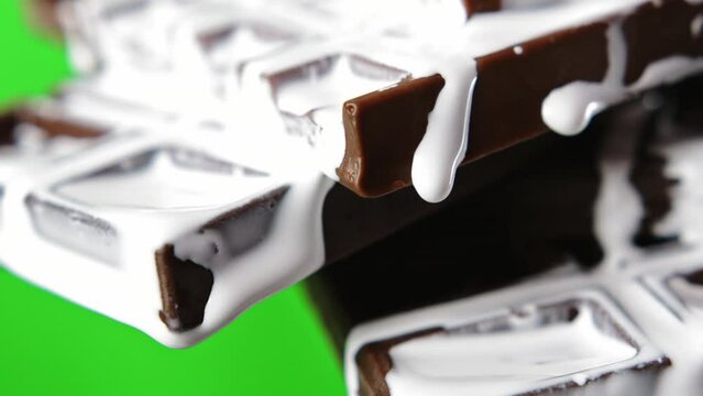 Close-up of chocolate with white cream. Stock clip. White liquid cream flows down chocolate bar. Sweet chocolate with cream on green background