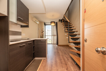 kitchen in a loft with dark wood furniture combined with white and light oak carpentry, a window in the background and a staircase with wooden steps and a metal structure
