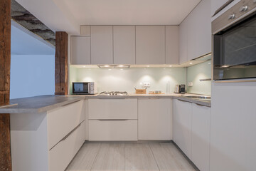 Kitchen with modern furniture covering three walls with integrated appliances and vintage wooden columns