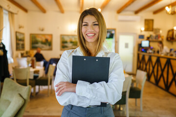 One woman young adult caucasian standing and smiling in the restaurant or hotel with paperwork in her hands and waiting clients Entrepreneur manager business modern lifestyle concept