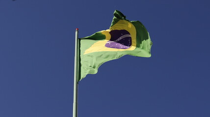 Bandeira do Brasil tremulando ao vento com céu azul ao fundo.