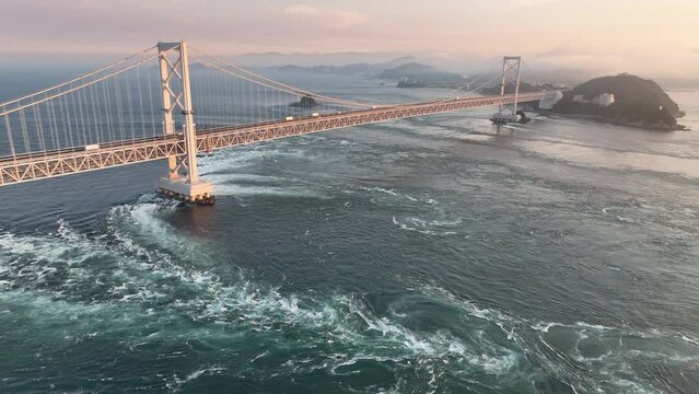Slow aerial pullback and rise over strong current under bridge at sunset