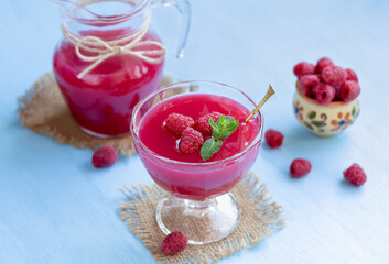 Raspberry kissel in a glass. Traditional russian berry drink or dessert made from fresh berries, water and corn starch. Glass of cold raspberry cocktail with fresh berries and jug on background.