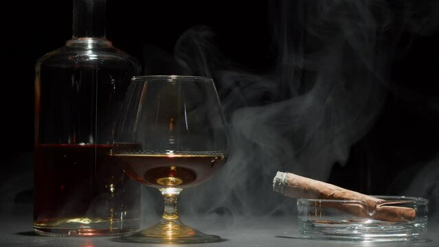 Brandy or whiskey and cigar close-up. Smoking cigarette and drinking luxury cognac on black background. Alcohol amber drink, rum, liqour beverage in glass.
