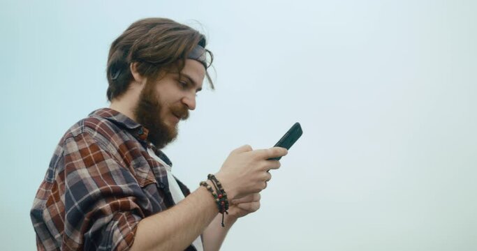 Young hypster man chats with someone on his phone standing on the top of the rock before beautiful mountain view covered with fog