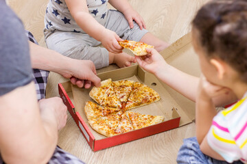 Family hands taking pizza slices on wooden floor background.