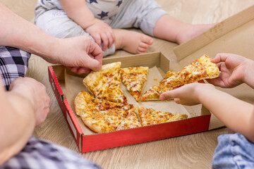 Family hands taking pizza slices on wooden floor background.