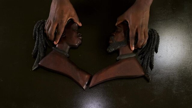 Top down shot of an African American man's hands placing a male and female wooden African masks side by side on a brown table