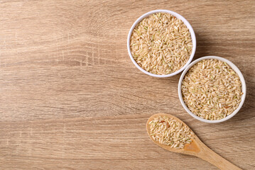 Thai brown rice seed in bowl with spoon on wooden background, Organic rice grain, Table top view