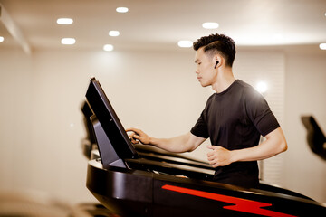 Fototapeta na wymiar Asian young man in sportswear running on machine treadmill at fitness gym. Concept for exercising, fitness, and healthy lifestyle.