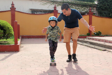 Latin single dad teaches his son to ride a skateboard with a helmet very funny and happy of the...