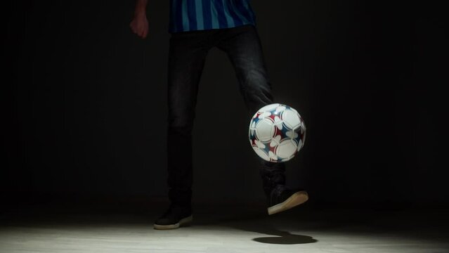 Professional football player throwing ball close-up. Sportsman portrait, training soccer in studio. Sports school concept. Young man playing, practicing on black background.