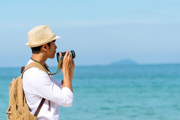 Man traveler using digital camera on summer beach blue sky take a photo. Asian Photographer man...