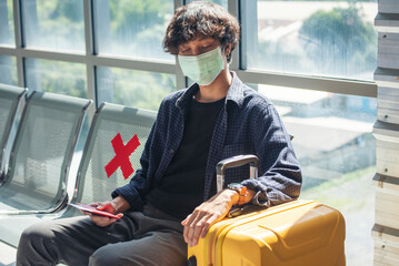 Asian young man traveller new normal wearing face mask sitting Social distancing holding smartphone...
