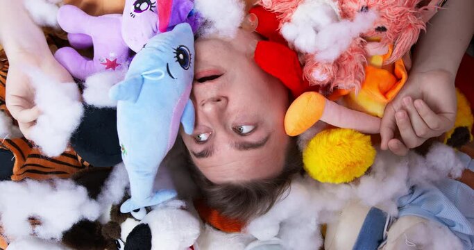 Plump man lies on heap of different plush toys. Scared man spits stuffing from soft animals out of mouth. Mess at home created by dogs close upper view
