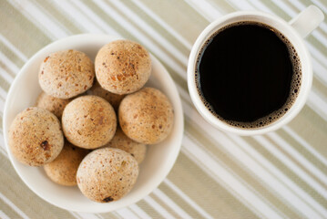 Lay flat view of white bowl filled with brazilian cheese bread and a mug of black coffee - pao de queijo integral, cafe preto (Brazilian Food)