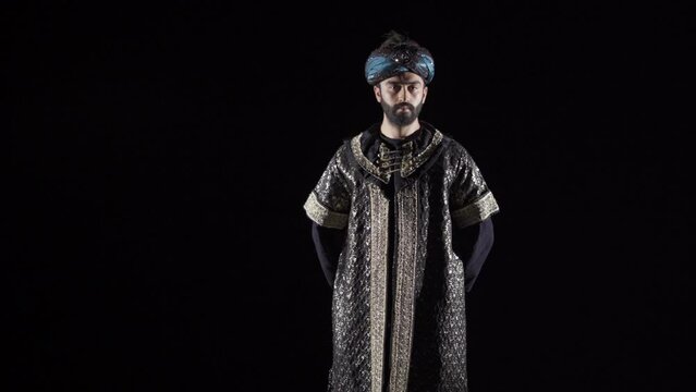 Ottoman Sultan in the Middle Ages. Black background.
The sultan straightens his clothes by looking at the camera.
