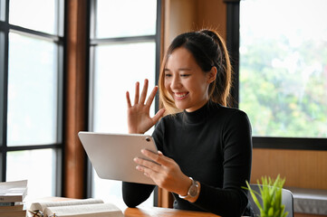 Charming young Asian female freelancer having an online meeting via digital tablet.