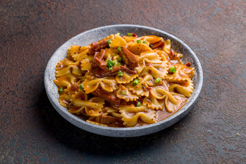 Farfalle with stewed beef on grey plate on dark table