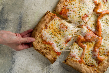 hand takes pizza margarita, square pizza top view on stone table