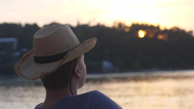 Young man in hat looks at sunset relaxes on the beach