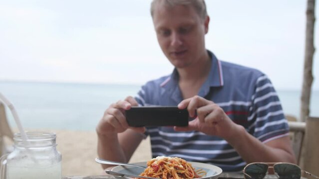 Man takes a picture with a smartphone camera of bolognese pasta in tomato sauce with basel leaves in a beach cafe