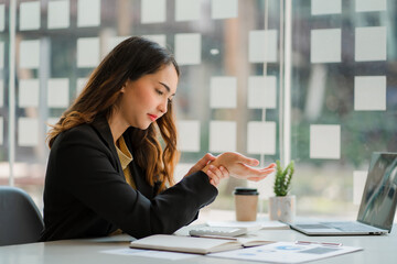a businesswoman sitting at a desk in the office touching her wrist feeling pain from using the...