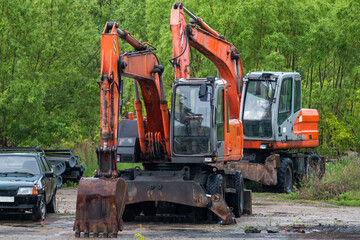 Two orange wheeled excavators near green forest