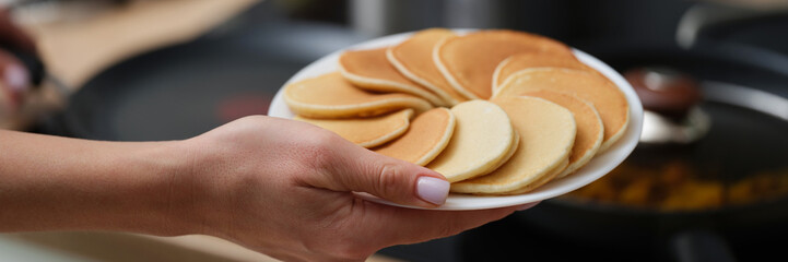 A woman's hand holds a white plate of pancakes